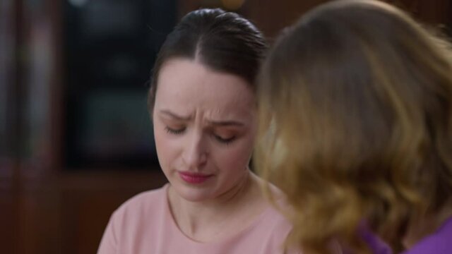 Rack focus from charming young beautiful crying woman grieving to caring mother hugging supporting daughter. Close-up of Caucasian women talking and embracing at home indoors. Stress and unity