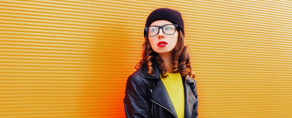 Portrait of beautiful young woman wearing a black leather jacket and hat, yellow sweater on an orange background