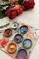desk with palette full of colored paint, brush and bouquet of colorful roses, art and decoration objects, studio
