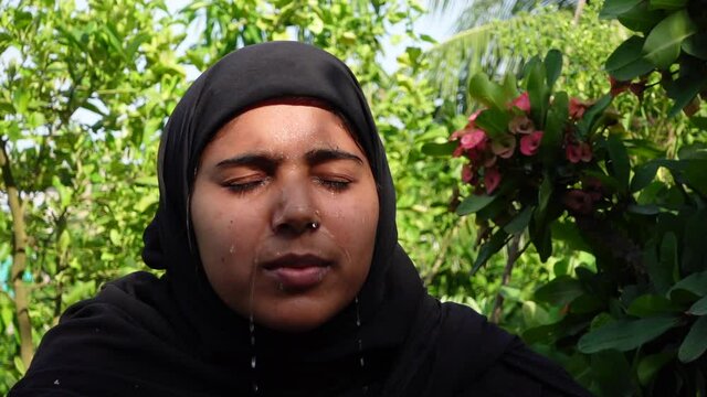 A woman splashes cold water on her face on a hot day. A Muslim woman dressed in black is performing ablution with water. The concept of cleaning the face with water. Slow-motion video. 