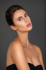 Naklejka premium Portrait of a sexy young white woman with wavy hair in a bun and beautiful makeup and lipstick posing by herself inside a studio with a grey background.