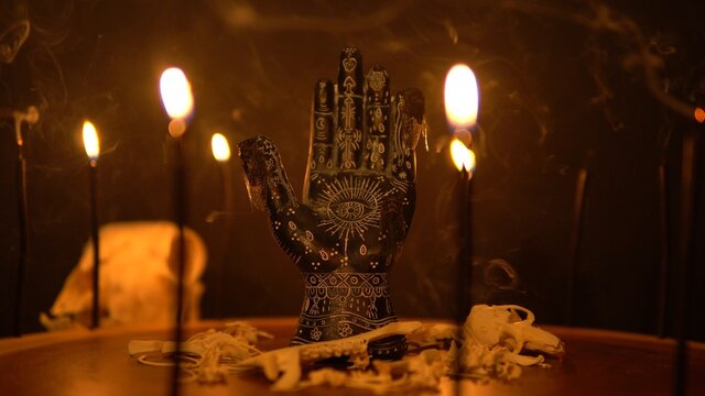 Mystical esoteric table with ritual objects. Fortune teller palm with black candles and animal bones on tree trunk surface. Prediction destiny and forecasting future hand reader statue.