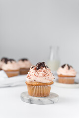 Vanilla cupcake with a tall swirl of pink frosting, chocolate glaze and a cookie, plain cupcake with pastel pink buttercream with chocolate and cookie garnish