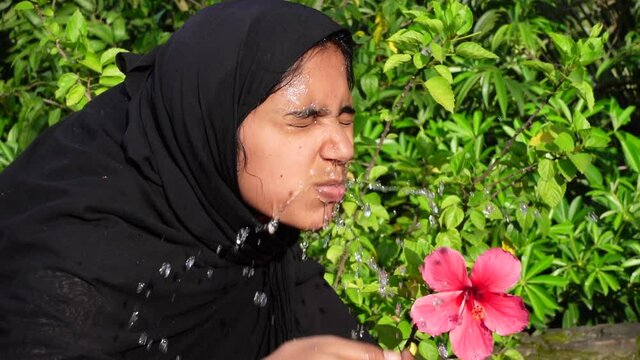 A woman splashes cold water on her face on a hot day. A Muslim woman dressed in black is performing ablution with water. The concept of cleaning the face with water. Slow-motion video. 