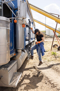 Female farmer climbing ladder of semi truck tractor trailer on farm