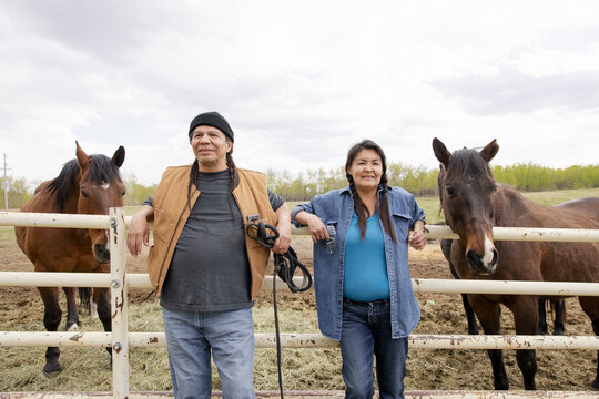 Portrait confident farmers with horses at paddock fence on farm
