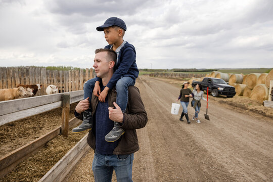 Farmer father carrying son on shoulders on rural farm