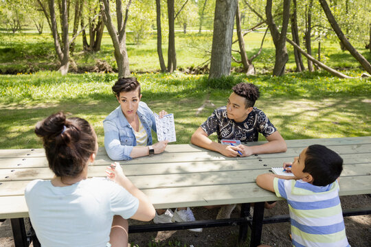 Mother Teaching Children With Guidebook At Park Table