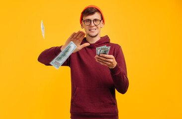 handsome guy wearing orange hat with glasses and red sweatshirt, throws one dollar bill, concept: successful young man