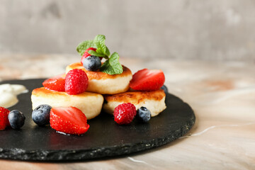 Slate plate with tasty cottage cheese pancakes and berries on grunge background
