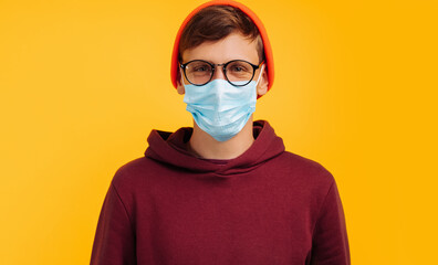 handsome man in a protective mask. in glasses and an orange hat and a red sweatshirt, smiling at camera