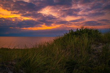 Blazing sunset with dramatic cloudscape over the grassy sand dunes in the shore on Cape Cod