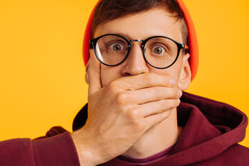 man covered his mouth with his hand, a frightened man, in an orange hat and red sweatshirt, and glasses