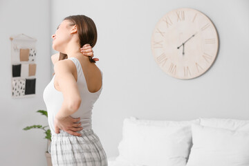 Young woman suffering from back pain in bedroom