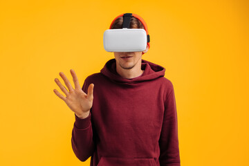 happy man in virtual reality glasses, stretches his hand, plays games, in an orange hat and a red sweatshirt