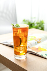 Glass of tasty ice tea with lemon on table in room