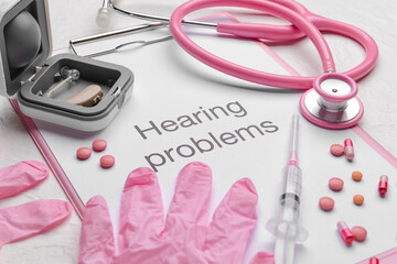 Clipboard with text HEARING PROBLEMS, stethoscope and gloves on white background