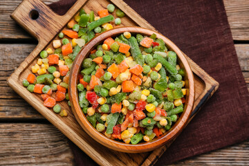 Bowl with mix of frozen vegetables on wooden background, closeup