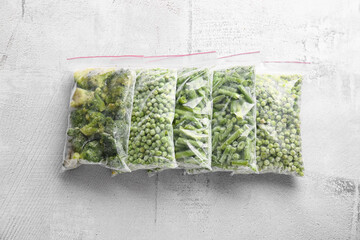 Plastic bags with different frozen vegetables on grey background
