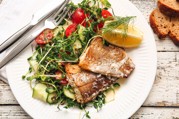 Plate with tasty baked cod fillet and vegetables on light wooden background