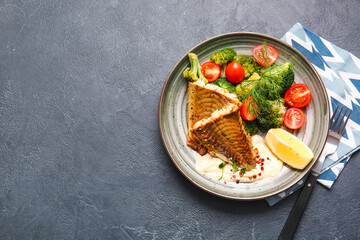 Plate with tasty baked cod fillet and vegetables on dark background