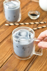 Woman holding glass cup of tasty Charcoal Latte on wooden background