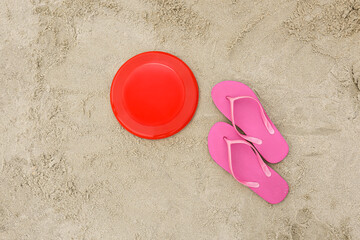 Fototapeta na wymiar Frisbee disk and flip-flops on sand