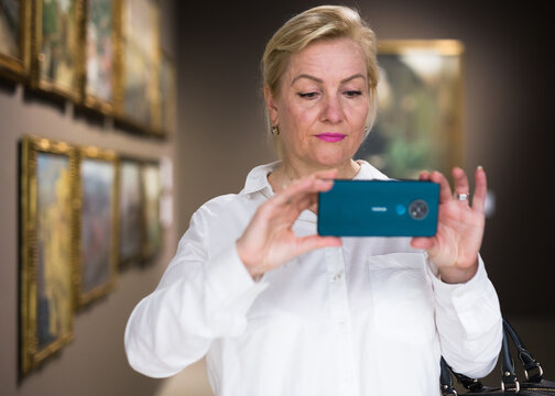 Female visitor taking picture in art gallery, using smartphone