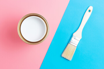 Open paint can and paintbrush on blue and pink background top view.