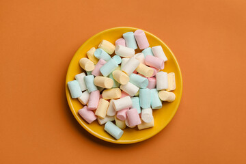 Plate with sweet marshmallows on orange background