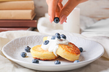 Woman decorating cottage cheese pancakes with berries on table, closeup