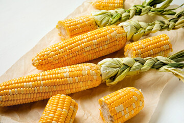 Fresh corn cobs and parchment on white table, closeup