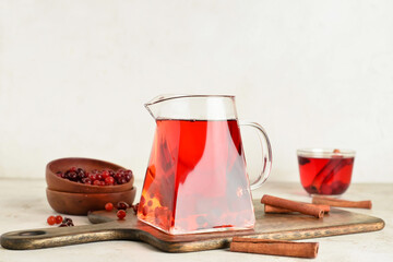Jug of tasty tea with cranberry on light background