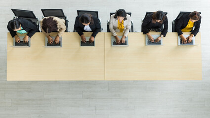 Table top view of six Asian business women sitting and working on laptops in straight line on wooden conference table in office. Concept for business meeting