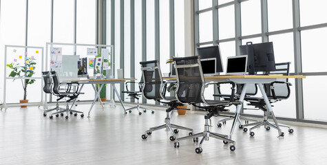 Meeting room with multiple glass windows and conference tables with laptops and desktops on in office