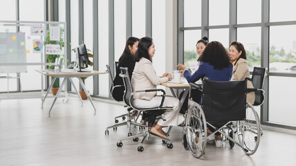 Asian business women and handicap woman sitting on wheelchair are in meeting together on the table...