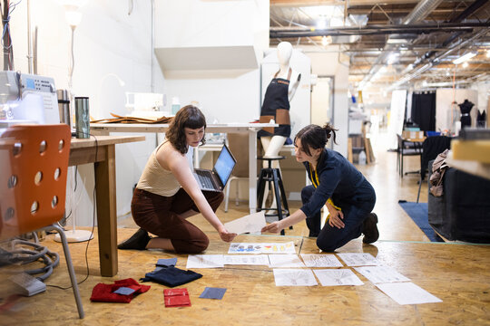 Female fashion designers reviewing sketches on studio floor
