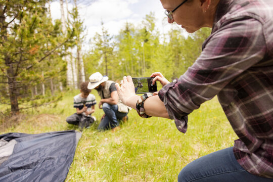 Woman taking photo of family putting up tent in forest