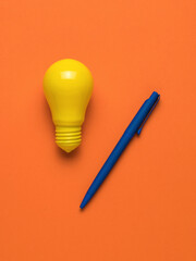 A blue pen and a bright yellow light bulb on an orange background. Flat lay.