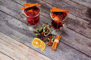 Mulled wine, two glasses of hot red wine with spices and orange slices are on a wooden table.