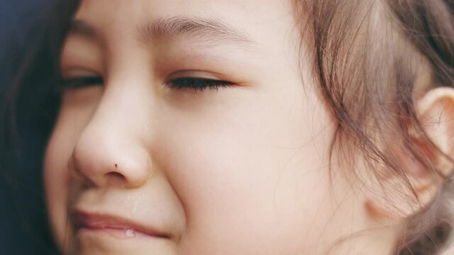 Face close up 4K of adorable 5 years old asian girl is crying in mother's holding hug and expressing people emotion of sadness, unhappiness, depression and grief through her eyes.