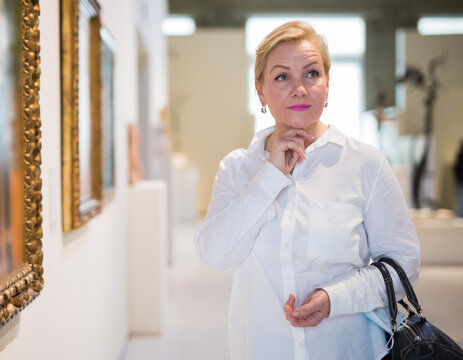 Adult woman visitor enjoying at exhibition, standing near pictures in museum of arts