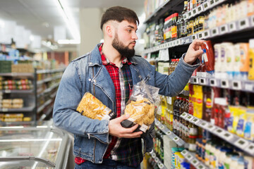 Serious bearded guy choosing products for dinner in grocery store.