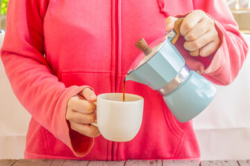 Woman in pink sweater pouring coffee from Moka Pot