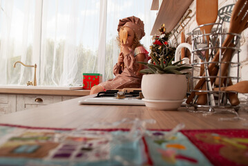 a little cute blonde 5 years old sitting on the kitchen table at home in the kitchen for the new year, cook's day or Christmas in the background of the tree