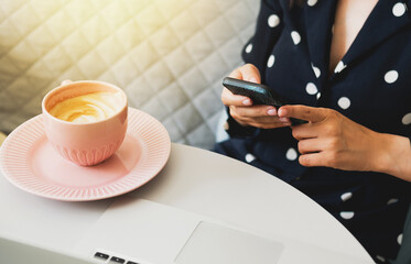 Beautiful woman sits in a cafe, drinks coffee, works on a computer and uses a phone