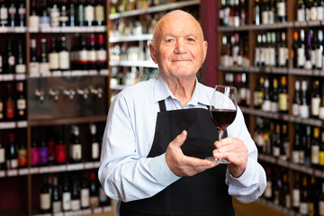Confident elderly male winemaker inviting to wine house, offering glass of wine for tasting. High quality photo