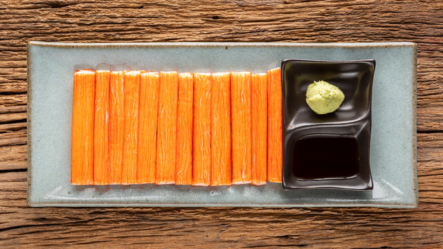 imitation crab sticks with wasabi and shoyu soy sauce in ceramic plate on rustic natural wood texture background, top view
