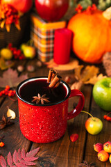 Obraz na płótnie Canvas red mug with mulled wine. Cinnamon sticks stick out of the cup and a star of star anise floats. Fruits and spices are all around on a wooden table