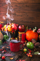 red mug with mulled wine. smoke comes from the mug. Cinnamon sticks stick out of the cup and a star of star anise floats. Fruits and spices are all around on a wooden table
